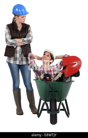 craftswoman accusing her lazy colleague for sitting in a wheelbarrow Stock Photo