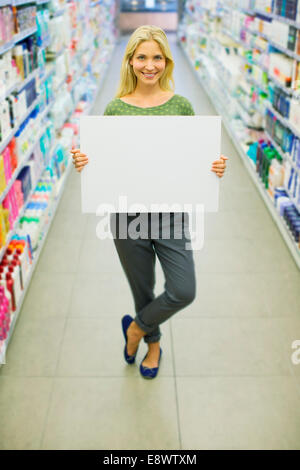 Woman holding blank card in grocery store aisle Stock Photo