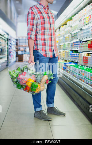 Man carrying full shopping basket in grocery store Stock Photo