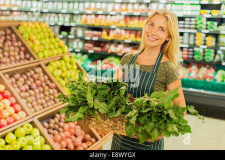 Clerk carrying basket of produce in grocery store Stock Photo