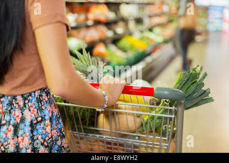 Close up of woman pushing full shopping cart in grocery store Stock Photo