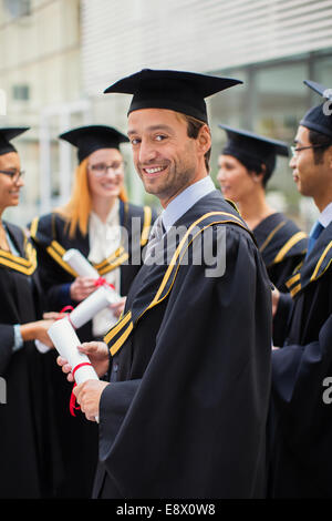 Student in cap and gown standing with friends Stock Photo