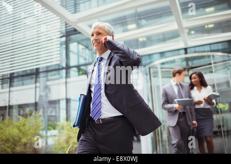 Businessman talking on phone while walking out of office building Stock Photo