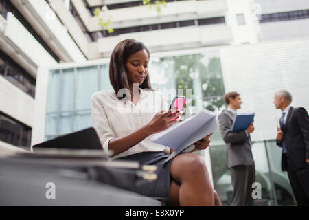 Businesswoman sitting on bench using cell phone outside Stock Photo