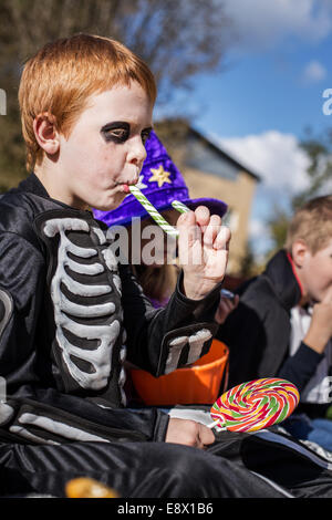 Red haired child with skeleton costume eating colorful candy. Halloween Stock Photo