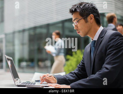 Businessman working on laptop outside of office building Stock Photo