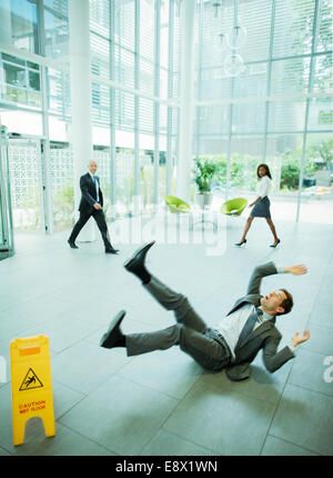 Businessman slipping on floor of office building Stock Photo