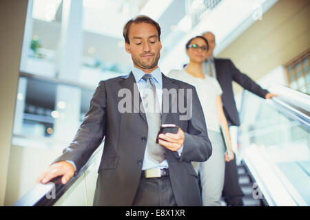 Businessman using cell phone on escalator in office building Stock Photo