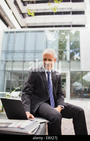 Businessman using laptop on bench outside of office building Stock Photo