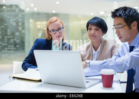 Business people gathered around laptop in office building cafe Stock Photo