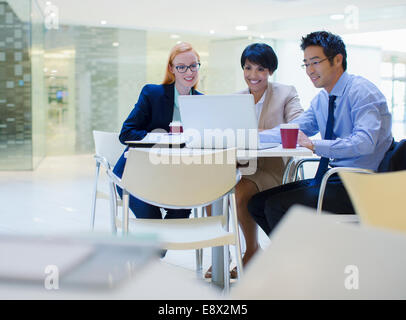Business people gathered around laptop in office building cafe Stock Photo