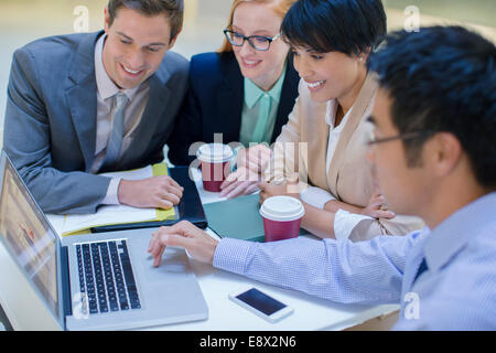 Business people gathered around laptop in office building cafe Stock Photo