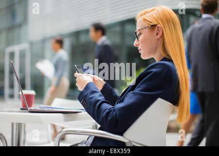 Businesswoman using cell phone at table outside Stock Photo