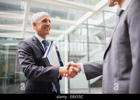 Businessmen shaking hands in office building Stock Photo