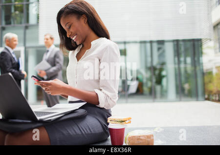 Businesswoman sitting on bench using cell phone Stock Photo