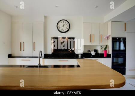 A modern cream kitchen inside a home in the UK showing an angled wooden breakfast island. Stock Photo