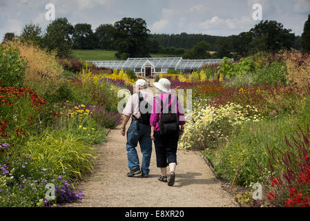 Summer visit to Helmsley Walled Garden & 2 visitors (couple) walk on path, looking at beautiful flowers on borders - North Yorkshire, England, UK.