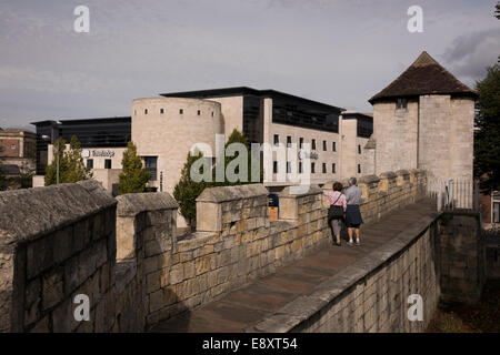 People on historic city walls wall-walk by ancient Fishergate Tower (modern architecture of Travelodge hotel beyond) - York, North Yorkshire, England. Stock Photo