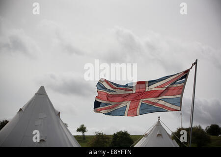A vintage ww1 period Union Jack British flag flying at full mast, with two canvas army camping tents in the background. Stock Photo