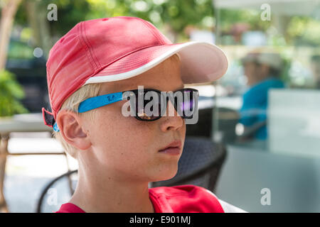 Portrait of a 13 year old boy wearing a base-cap and sunglasses in the town of Kos, Greece Stock Photo