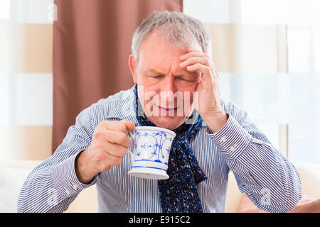 Old man drinking tea to cure bad cold or flu at home Stock Photo