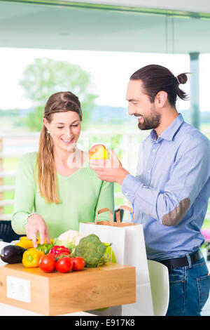 Man and woman unpacking fruits and vegetables out of grocery shopping bag in home kitchen Stock Photo