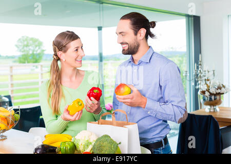 Man and woman unpacking fruits and vegetables out of grocery shopping bag in home kitchen Stock Photo