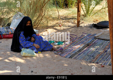 Bedouin woman sitting on traditional carpet in shade Stock Photo
