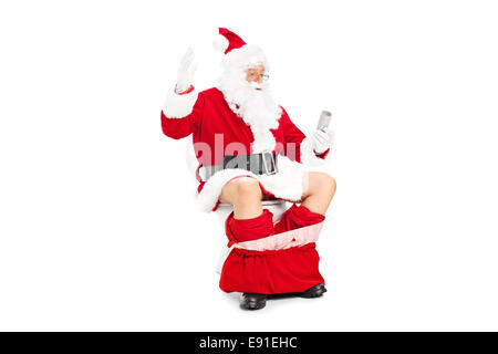 Santa looking at an empty toilet paper roll seated on a toilet isolated on white background Stock Photo