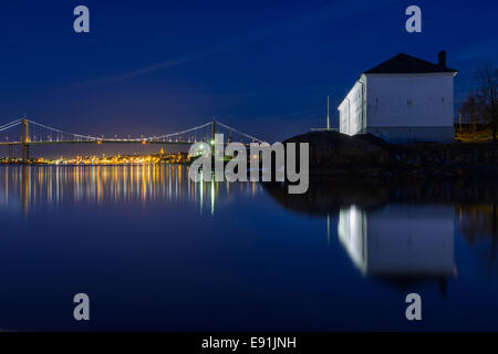 Illuminated bridge over a still river with a city lit up in the background Stock Photo