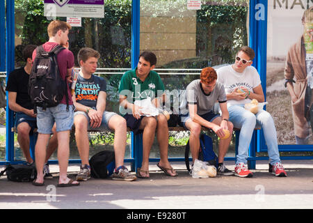 Group of lads sat eating whilst waiting at bus stop in Krakow, Poland Stock Photo