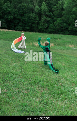 Young Boy in Dragon Costume Playing with Young Girl in Princess Costume in Grassy Field Stock Photo