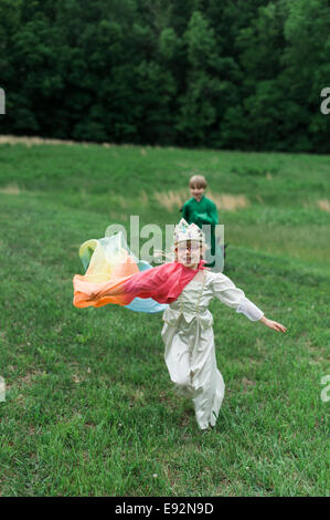 Young Boy in Dragon Costume Playing with Young Girl in Princess Costume in Grassy Field Stock Photo