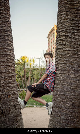 teenage boy climbing between tow palm tree's Stock Photo