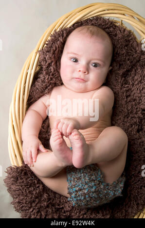 9 month old baby boy in a basket, laying on his back playing with his feet Stock Photo