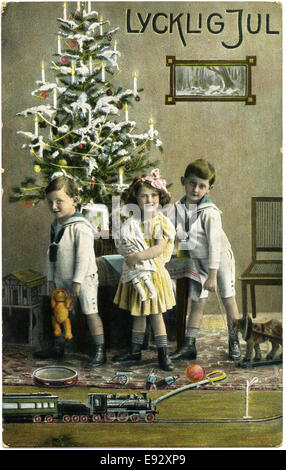 Three Children with Presents and Train Set in Front of Christmas Tree, 'Lycklig Jul', Postcard, Sweden, circa 1912 Stock Photo