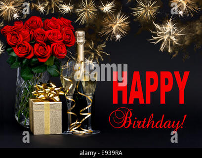 red roses, bottle of champagne, golden gift with beautiful fireworks on black background. card concept with sample text Happy Bi Stock Photo