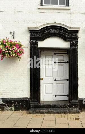 white and black classical door  on white painted bricks facade with a bucket of flowers nearby, shot in touristic village on riv Stock Photo