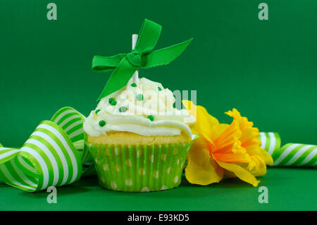 Beautiful green decorated cupcake with daffodil and stripe ribbon on green background for Spring, St Patricks Day Stock Photo