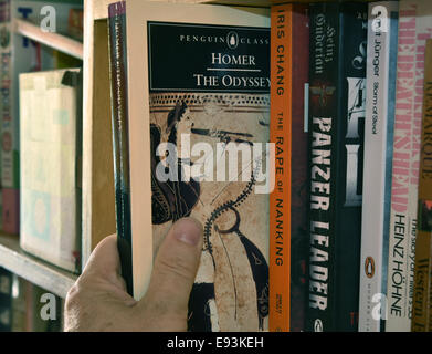 A hand removing a copy of Homer's The Odyssey from a bookshelf Stock Photo