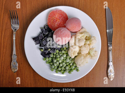 knife and fork  and heap of frozen black currant covered with hoarfrost in the white plate Stock Photo