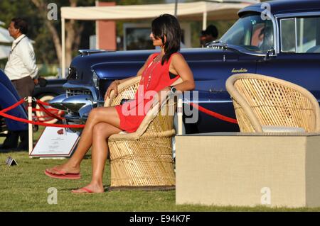 A young woman in a summer dress sits on a wicker chair at a classic car concours in Delhi, India Stock Photo