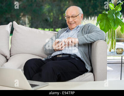 Happy Senior Man Text Messaging Through Smartphone At Porch Stock Photo