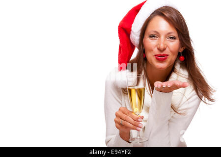 Playful woman wearing a festive red Santa hat and holding a flute of champagne celebrating Christmas blowing a kiss across the p Stock Photo