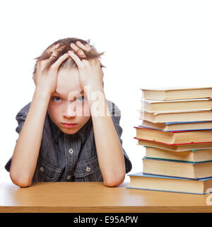 Portrait of upset schoolboy sitting at desk with books holding his head Stock Photo