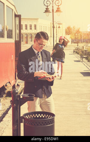 Beautiful vintage style couple outside retro train coach have a romantic encounter while he reading  book and she race toward hi Stock Photo
