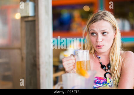 Young woman drinking beer in outdoor bar looking away making funny face Stock Photo