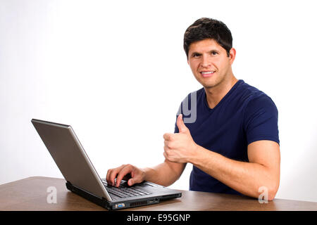 Young man smiles and gives a thumbs up sign after executing a successful internet transaction or purchase on a website from his Stock Photo