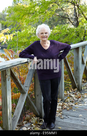 85 year old woman standing on dock ramp in Autumn landscape. Stock Photo