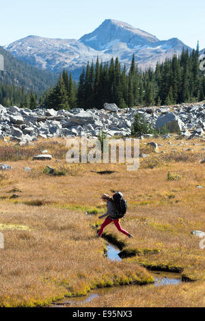 Woman crossing a small stream on a backpack trip in Oregon's Wallowa Mountains. Stock Photo